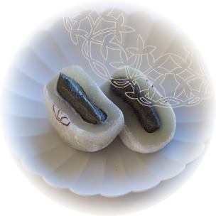 Mochis au sésame noir, coupés en deux dans une coupelle en papier à pétales, montrant une garniture foncée et riche.