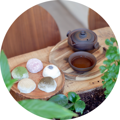 Un gâteau roulé sur une assiette en céramique, une théière et une tasse de thé sur une table en bois brut avec des plantes vertes.